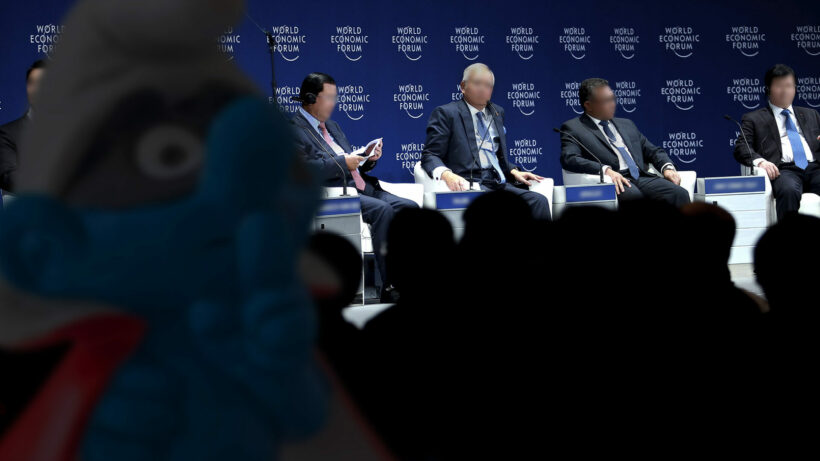 Photo collage showing a row of speakers at the World Economic Forum. A blurred shadowy figure in the foreground resembles a conspirator smurf.
