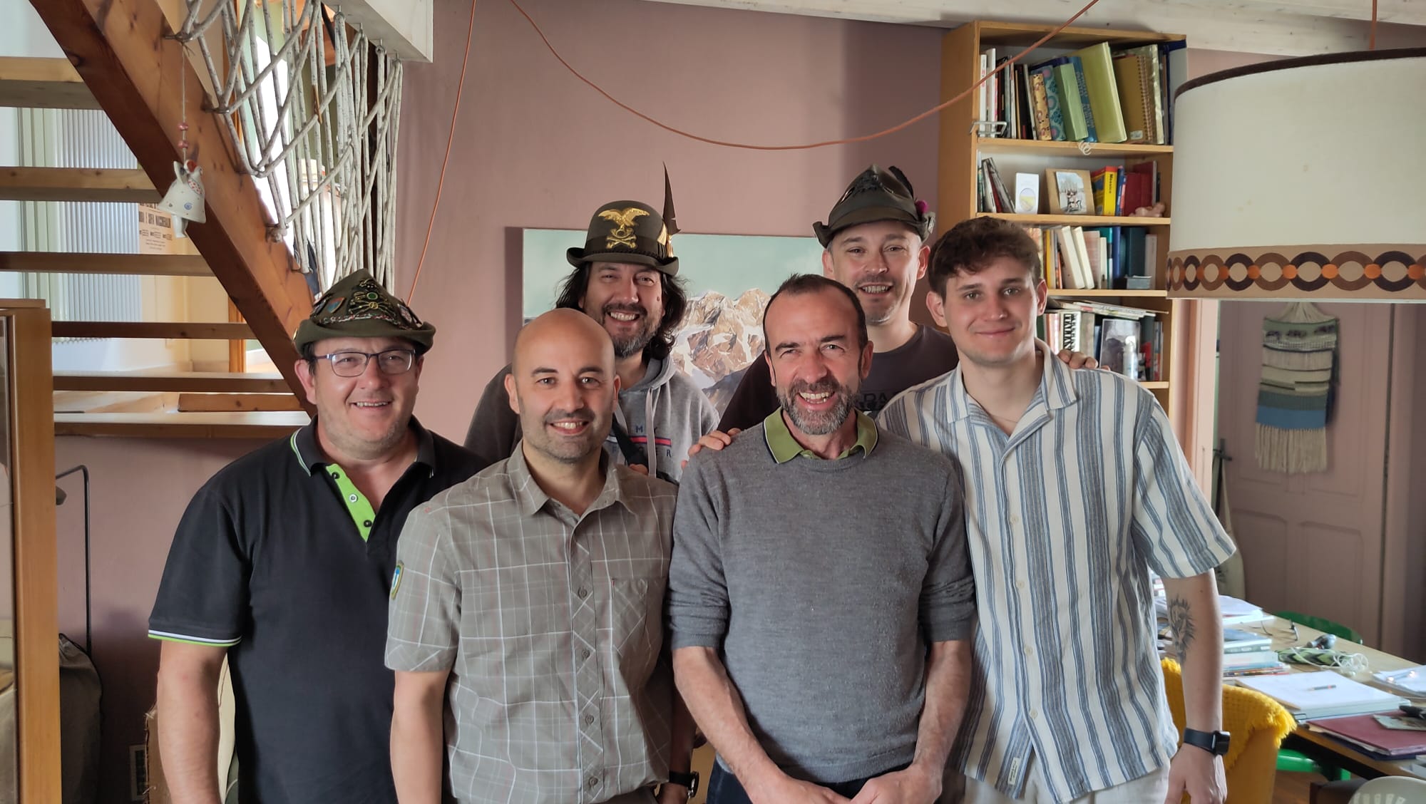 Stanza con gruppo di uomini alcuni con il cappello da alpino e sullo sfondo acquerello del Mont Rosa