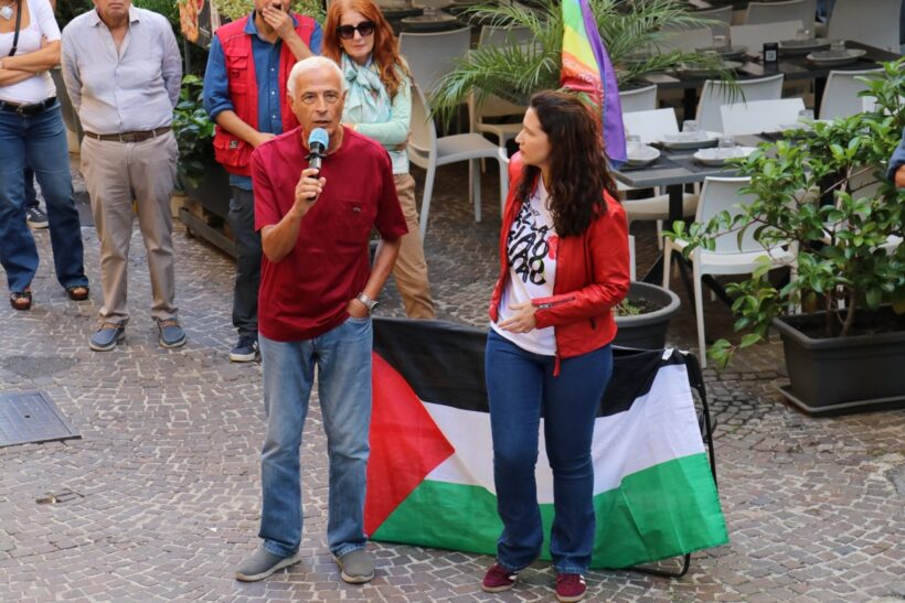 Ermete Ferraro parla al microfono durante una manifestazione pacifista a Napoli, davanti a una bandiera palestinese.