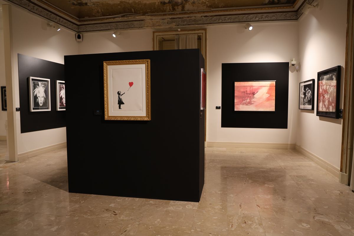 Veduta della mostra “Warhol vs Banksy – Passaggio a Napoli” a Villa Pignatelli. Al centro, “Girl with Balloon” di Banksy, in dialogo con opere di Andy Warhol.