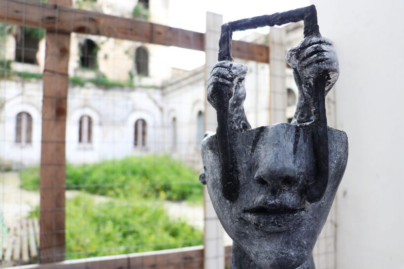 Una scultura contemporanea raffigurante un volto umano che solleva una forma simile a una porta o a una cornice. L’opera, collocata all’interno dell’ex complesso manicomiale di Aversa, suggerisce simbolicamente un gesto di apertura e di cambiamento di prospettiva, invitando a riflettere sul tema dello sguardo, della memoria e della trasformazione.