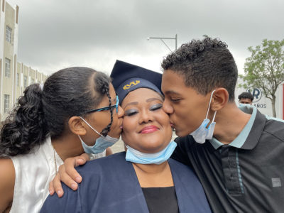 An adult student is congratulated by her two children at her high school graduation ceremony.