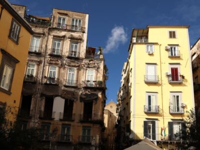 Uno scorcio urbano di Napoli mostra edifici residenziali ravvicinati, segnati da differenti condizioni di conservazione e da evidenti contrasti architettonici. L’immagine accompagna una riflessione sul diritto alla casa, sulle fragilità del tessuto urbano e sulle disuguaglianze che attraversano l’abitare contemporaneo.
