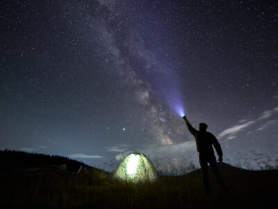 Viajero masculino brillando con una linterna en el cielo estrellado nocturno.